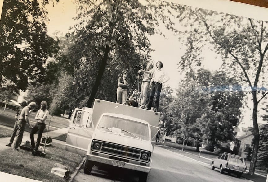 Black & white photo, circa 1970s, of a film crew w/ camera shooting from atop their box truck